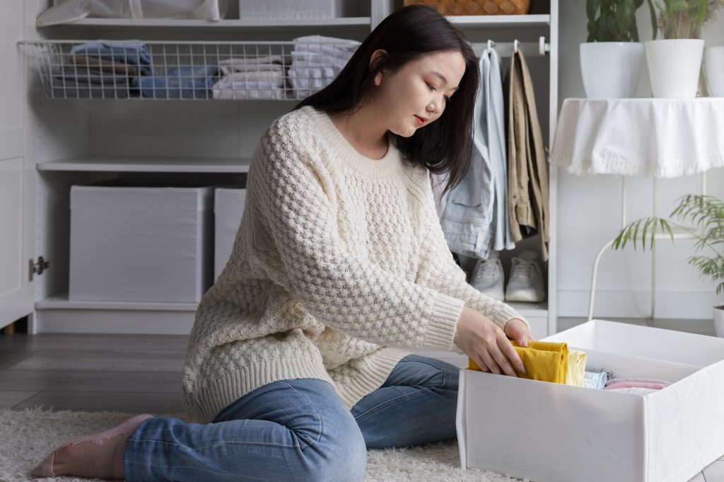 A woman organizing clothes in a storage box to optimize apartment space.